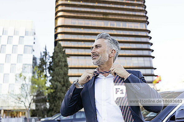 Mature businessman removing tie in front of building