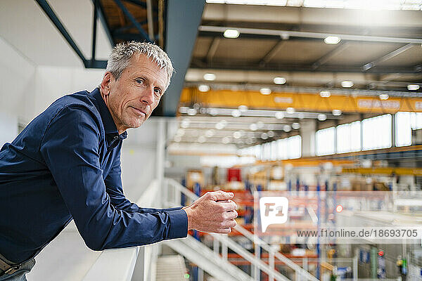 Mature businessman leaning on railing at factory