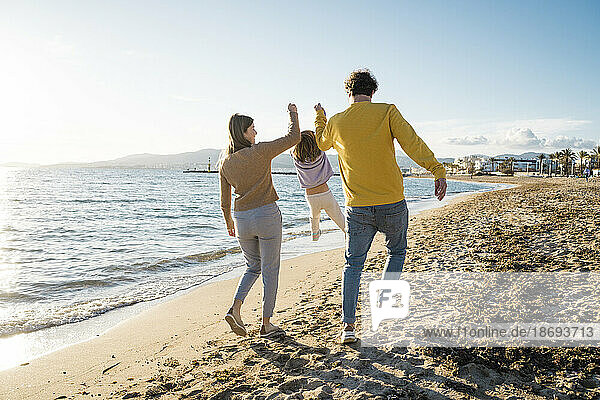 Father and mother picking up daughter walking on sand at beach