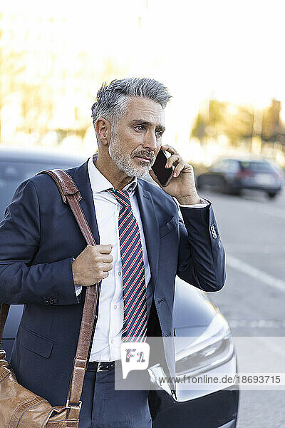 Geschäftsmann trägt eine Tasche und spricht mit dem Smartphone