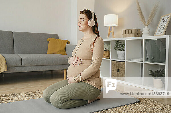 Schwangere Frau sitzt zu Hause auf der Trainingsmatte und hört Musik