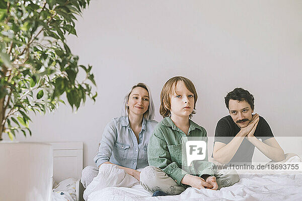 Lächelnder Mann und Frau mit Sohn sitzen zu Hause im Bett