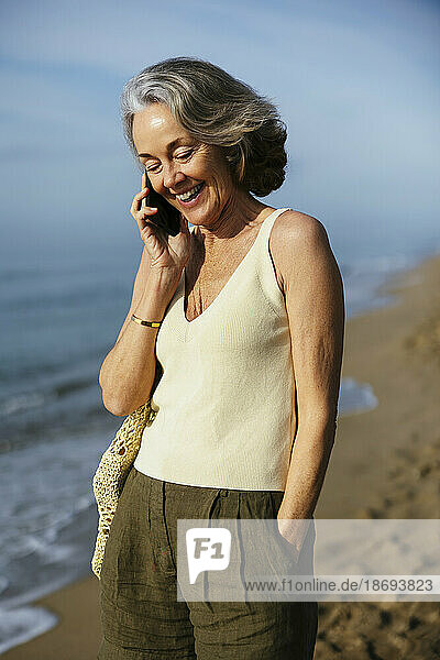 Glückliche Frau  die am Strand steht und mit ihrem Smartphone spricht