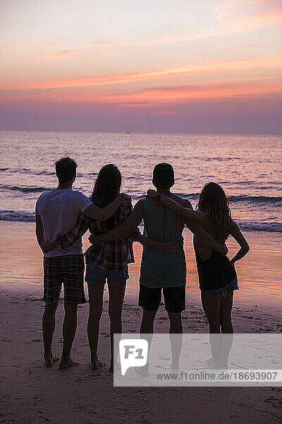 Friends with arms around looking sunset view at beach