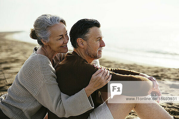 Lächelnde Frau umarmt Mann  der am Strand sitzt