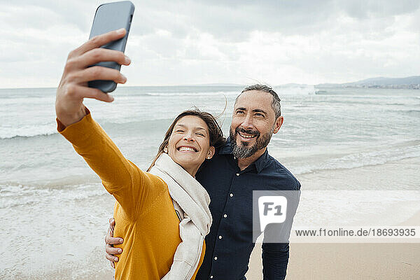 Glückliche Frau macht Selfie mit Mann per Handy am Strand