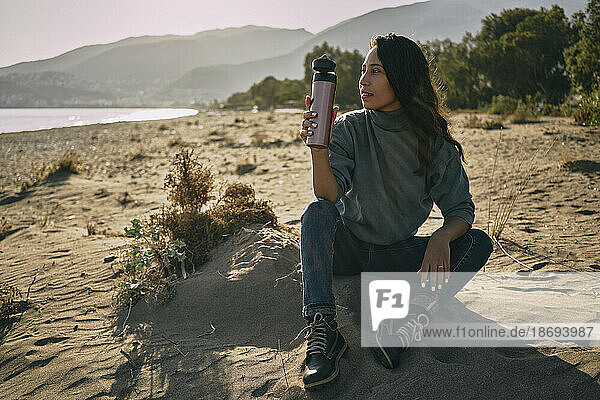 Woman holding water bottle sitting at beach