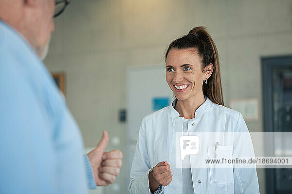 Happy doctor talking to senior patient through gestures at clinic