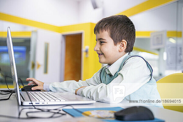 Smiling boy using laptop sitting at desk in school