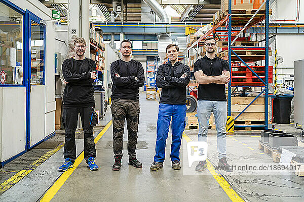 Confident employees with arms crossed standing in production hall at factory