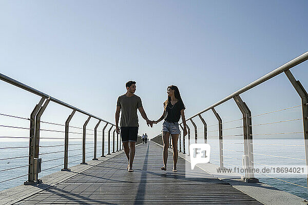 Young couple walking on bridge under sky