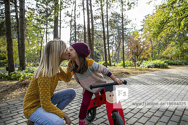 Daughter with bicycle kissing mother on footpath at park