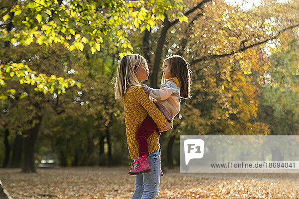 Mother carrying daughter in arms at autumn park