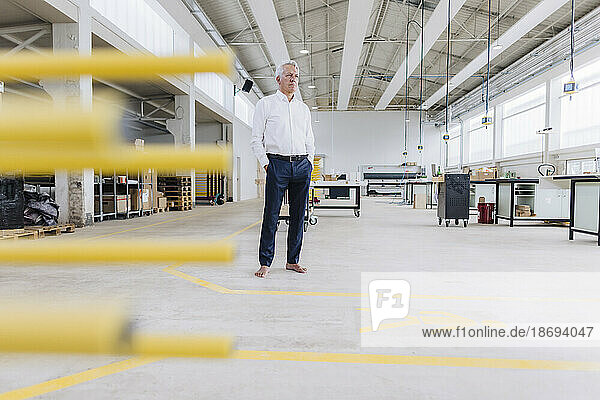Senior businessman with hands in pockets standing in factory