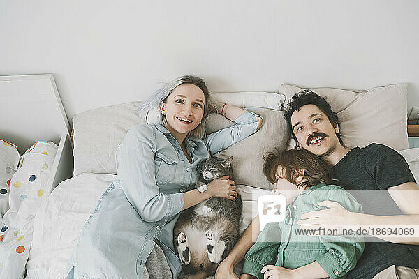 Happy family with cat relaxing on bed at home