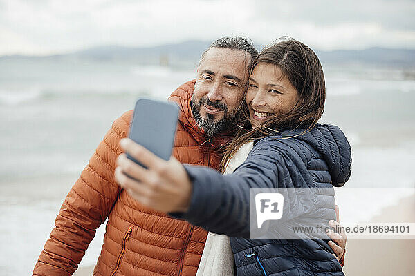 Glückliche Frau macht Selfie mit Mann per Smartphone am Strand