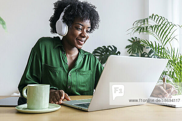 Smiling businesswoman wearing wireless headphones writing on note pad