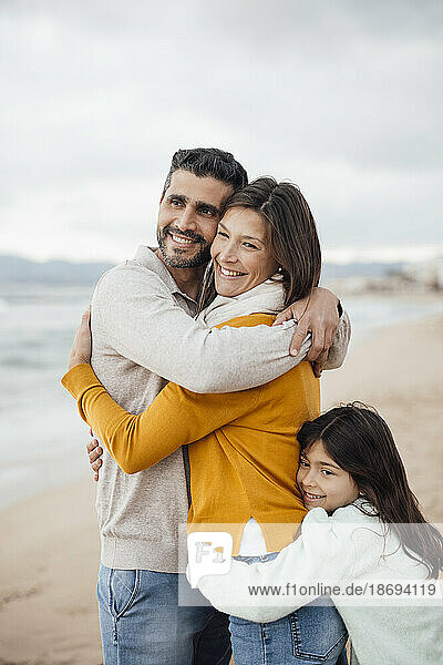 Happy man and woman with daughter hugging each other at beach