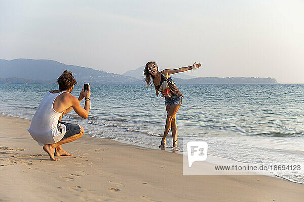 Man photographing girlfriend enjoying near shore at beach