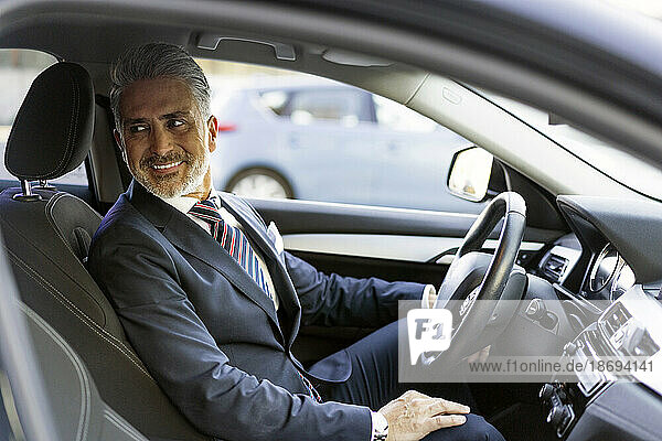 Smiling businessman sitting on driver's seat in car