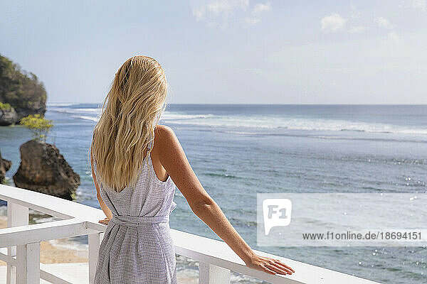 Blonde Frau blickt aufs Meer und steht neben dem Geländer