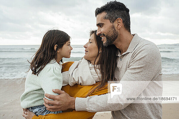 Smiling man with woman carrying daughter at beach