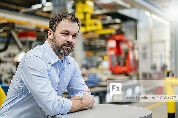 Smiling mature manager leaning on table at factory