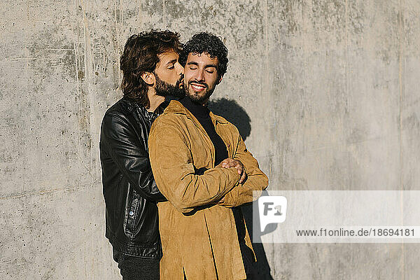 Gay man kissing boyfriend near concrete wall at sunny day
