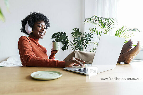 Happy businesswoman with coffee cup working on laptop at desk