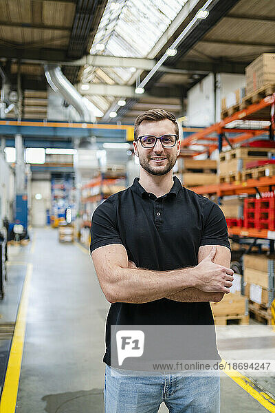 Employee wearing eyeglasses standing with arms crossed at factory