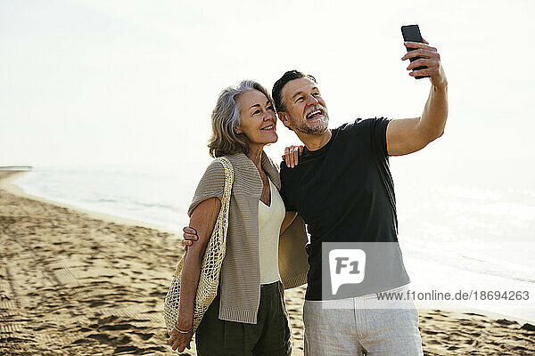 Man taking selfie with woman standing at beach