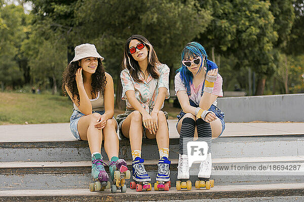 Lächelnde junge Freunde sitzen auf der Treppe im Park