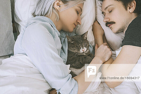 Couple with cat sleeping on bed at home