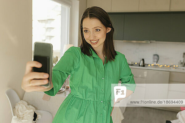 Woman with hand on hip taking selfie through smart phone at home