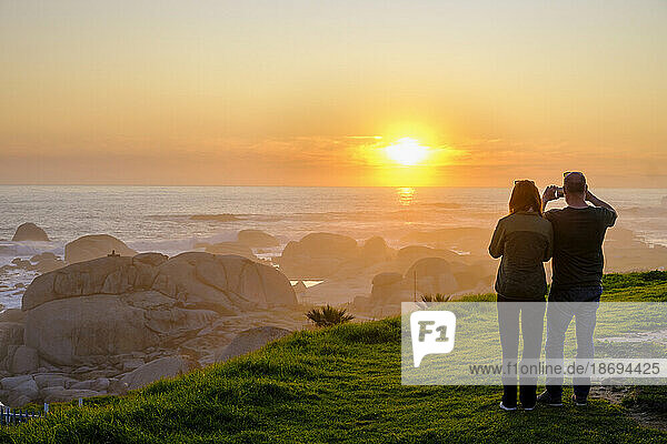 South Africa  Western Cape Province  Cape Town  Tourists photographing Atlantic Ocean at sunset