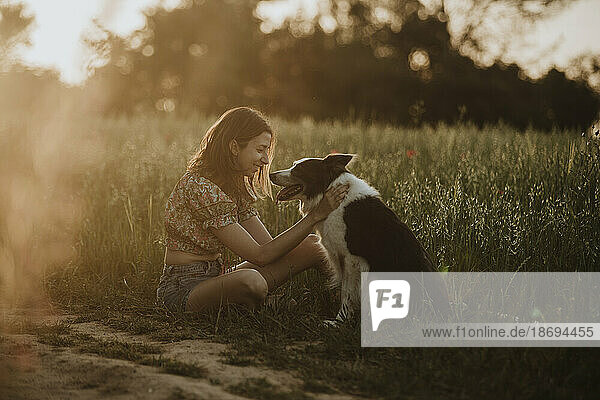 Smiling woman sitting with border collie dog in field