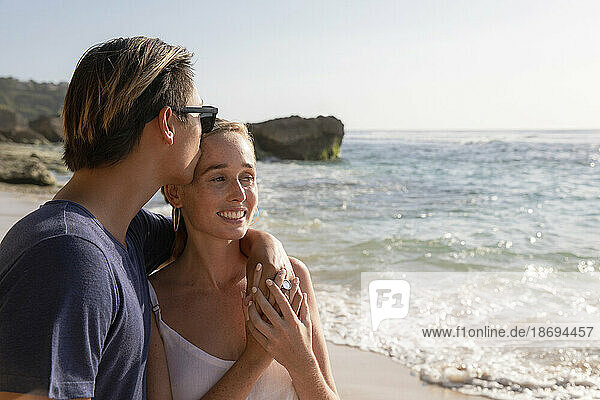 Mann küsst Frau am Strand auf die Stirn