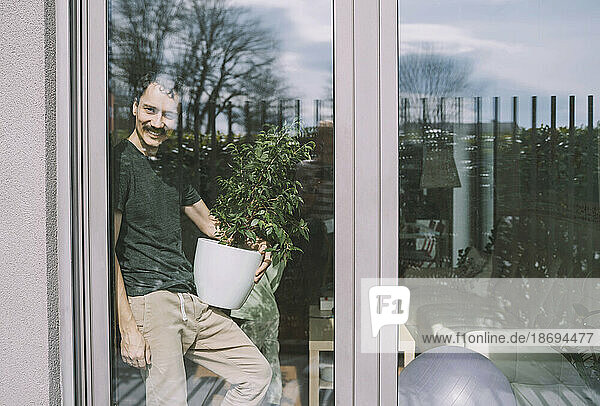 Smiling man holding plant seen through window