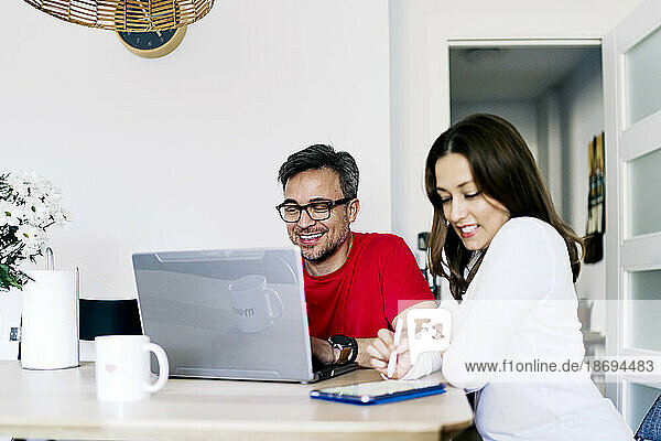 Man working on laptop sitting by woman using tablet PC at home