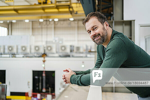 Lächelnder Mann lehnt an Geländer in Fabrik