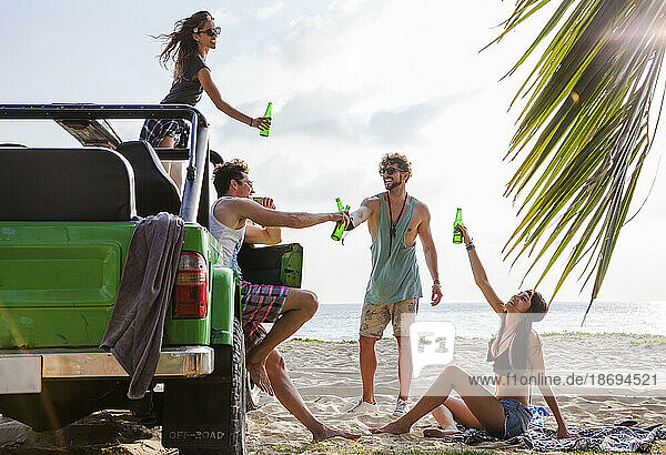 Fröhliche Freunde stoßen am Strand mit einem Geländewagen auf Getränkeflaschen an