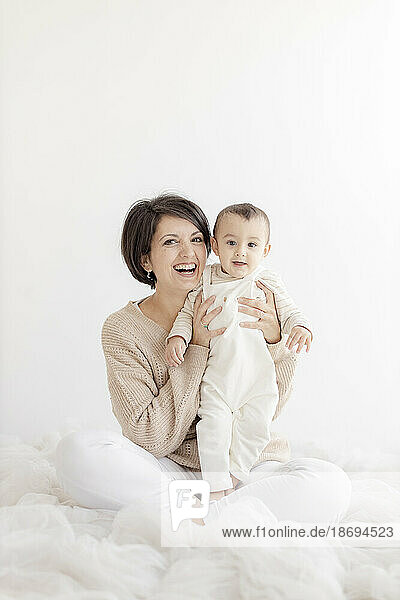 Happy woman sitting with cute son in front of white wall