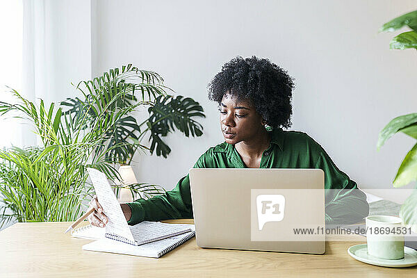 Geschäftsfrau mit Laptop liest Notizen am Schreibtisch