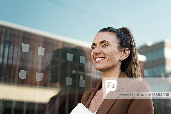 Happy young businesswoman near glass wall