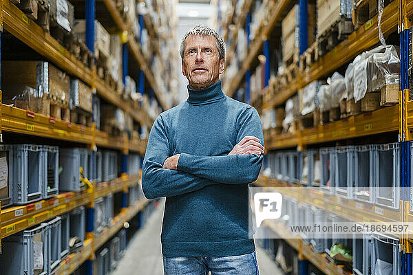 Thoughtful businessman with arms crossed standing in warehouse