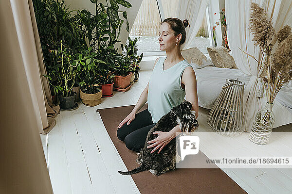 Woman practicing meditation with Schnauzer dog on exercise mat at home