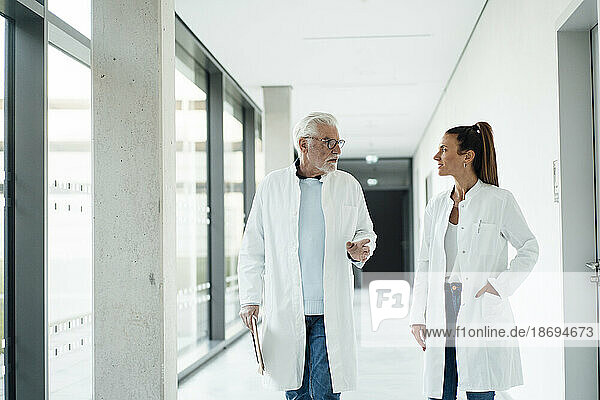Senior doctor discussing with colleague walking in hospital corridor