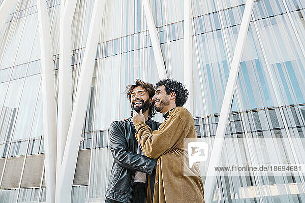 Happy affectionate gay couple standing in front of building