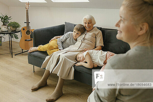 Grandmother sitting with grandchildren on sofa at home