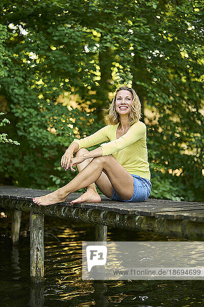 Smiling woman sitting on boardwalk at lake